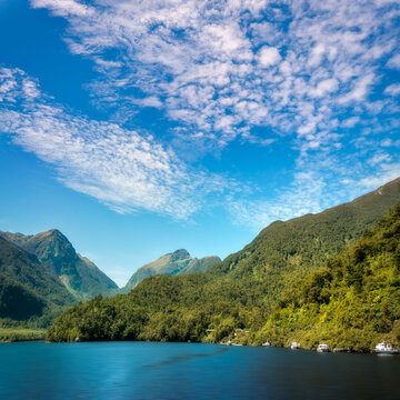 Wonderful view from the water with boats at Wanganella Cove in Doubtful Sound and with the mountain range in the distance that looks like a fantasy land in New Zealand, South Island.