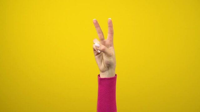 The female hand shows the sign of peace or victory. Studio photography on an isolated yellow background.