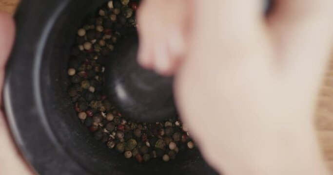 Woman grinds pepper seeds in black pestle and mortar hands close up
