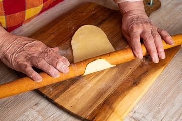 Woman rolling out the dough with a rolling pin on the kitchen table