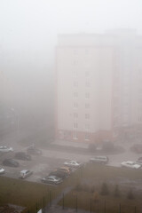 Foggy morning view from the roof of a tall building. Parking with cars near the apartments. Polluted air in the city