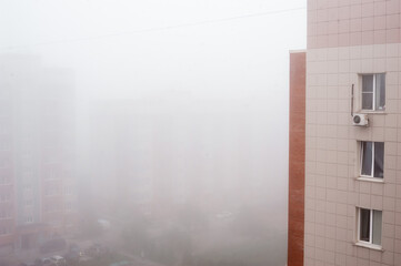 Foggy morning view from the roof of a tall building. Parking with cars near the apartments. Polluted air in the city