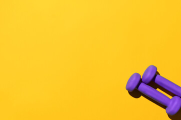 Dumbbells on a yellow background, copy space. Top view, flat lay. Two purple dumbbells for fitness and aerobics.