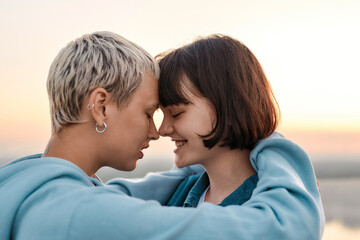 Fototapeta premium Close up of young loving lesbian couple hugging before kiss while admiring the sunrise together