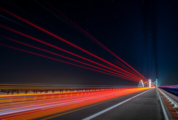 Fototapeta na wymiar light traces of cars driving along the road at night through a beautiful modern highway bridge