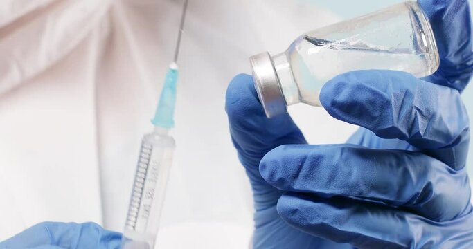 Close up of nurse hands holding a coronavirus, measles or flu vaccine, applying vaccine into the syringe. Medicine, science and healthcare