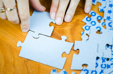Close-up of a girl hand collecting jigsaw puzzles on a wooden surface - 394603221