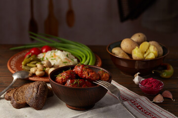 Meat balls in tomato sauce in a ceramic plate on a wooden table with potatoes and snacks. Rustic dinner with meatballs and snacks