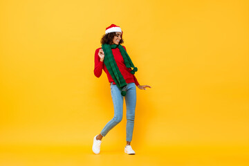 Fun portrait of happy African American woman in Christmas attire dancing on isolated yellow studio background