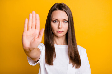 Photo portrait of serious girl showing stop signal with blurred palm isolated on vivid yellow color...