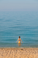 Attractive young woman in swimsuit stands waist-deep in the calm morning sea water