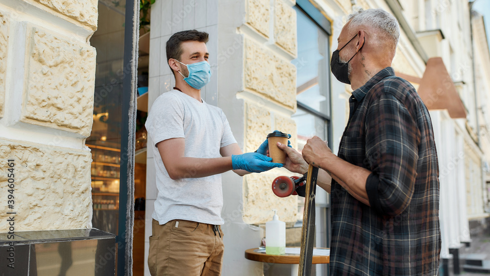 Wall mural Middle aged man wearing mask receiving hot coffee drink from hands of cafe assistant in protective gloves while collecting his takeaway order during coronavirus lockdown