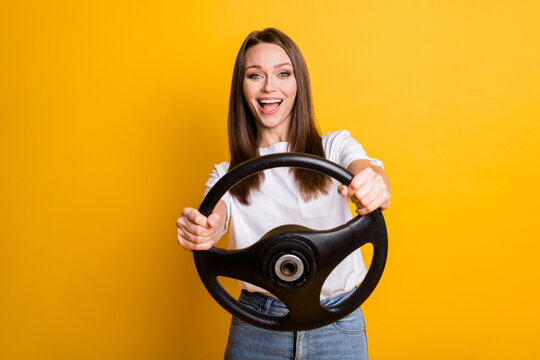 Photo portrait of pretty brunette girl keeping steering wheel learning to drive smiling isolated vibrant yellow color background