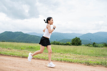 Happy Funny little asian girl fitness woman running at morning tropical forest trail. Athletic young child running in the nature. Healthy lifestyle.