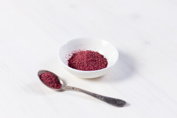 heap of ruby sumach spice powder in white bowl and spoon