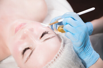 Naklejka premium Beautician in a beauty salon puts a protective mask on the client's face. Facial skin care and beauty treatments