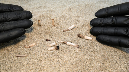 Man collecting used cigarette butts discarded on sandy sea beach,ecosystem habitat pollution