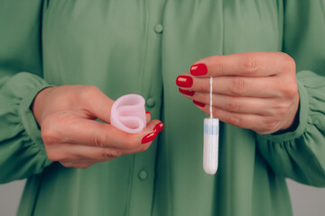 Close up of woman hand with perfect manicure, holding different types of feminine hygiene products - pink menstrual cup and tampons. Women health and hygiene concept, alternative hygiene products