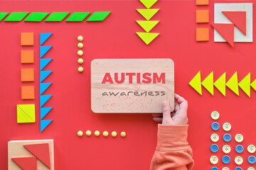 Creative design for Autism World Day, text on wood in hand. Tangram puzzle, flat lay on red.