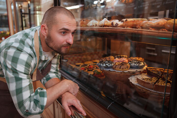 Young male baker working at his bakery, examining retail display