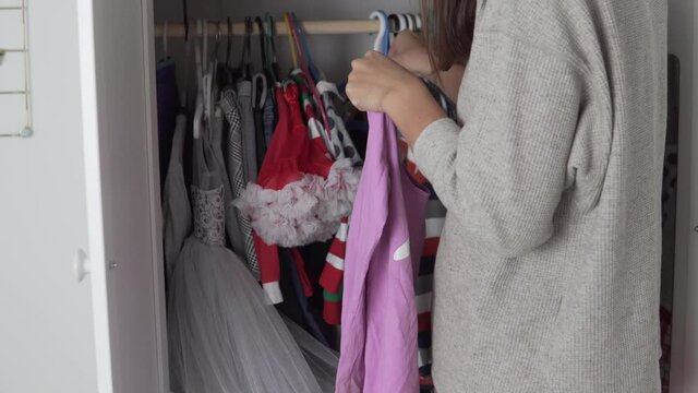 Housewife woman hangs clothes for Halloween in the closet of her little daughter at home.
