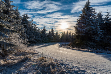 Late autumn mountain scenery with frozen trees, snow covered road and blue sky wirth few clouds