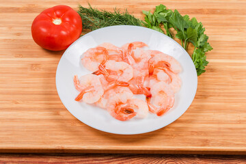 Cooked peeled prawn tails on the white dish against vegetables