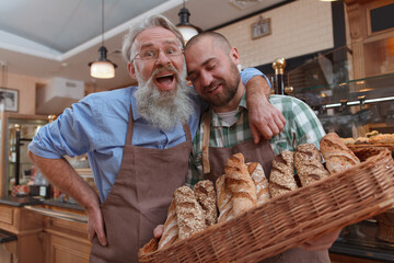Excited senior male baker laughing, hugging his son while working together at their bakery selling fresh bread