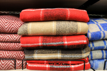 A stack of warm soft, wool plaids in a cage lies on a shelf in a wardrobe, store. Blankets for warmth and comfort in the supermarket in red, blue, yellow in winter