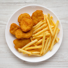Tasty Fastfood: Chicken Nuggets and French Fries on a plate on a white wooden surface, top view....