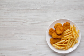 Tasty Fastfood: Chicken Nuggets and French Fries on a plate on a white wooden surface, top view. Overhead, from above, flat lay. Copy space.