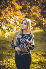 Woman girl long-haired blonde in an alley with trees with red leaves. She is happy confident in a...
