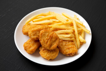 Tasty Fastfood: Chicken Nuggets and French Fries on a plate on a black background, side view.