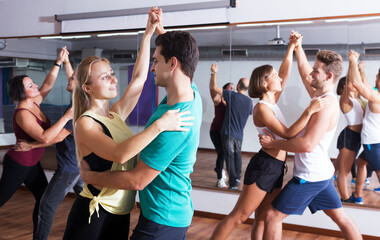 Fototapeta na wymiar Group of young glad people learning salsa at dance class. Focus on brunet man