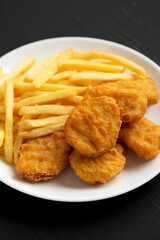Tasty Fastfood: Chicken Nuggets and French Fries on a plate on a black background, low angle view. Close-up.