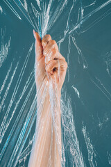 Plastic pollution. Ocean contamination. Save nature. Female volunteer hand collecting waste grasping transparent polyethylene film underwater isolated on teal blue background.