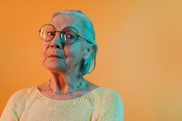 Smart elderly woman in round eyeglasses that gleam reflecting light looks down into camera. Old...