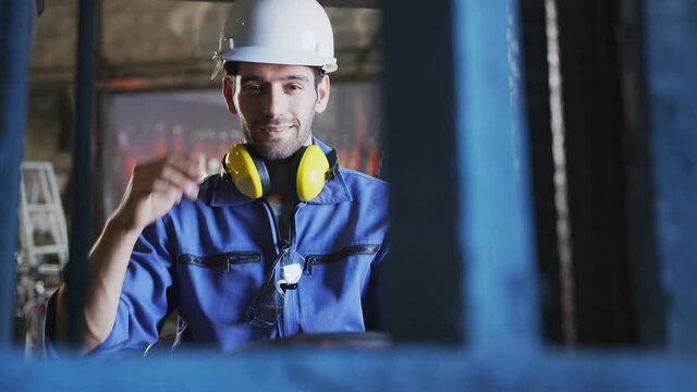 Concentrated forklift caucasian driver operating machine and holding hand on steering wheel  radio comminication operate teamwork with transportation of goods cargo in factory warehouse workshop.