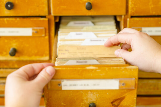 A female hand searching cards in old wooden card catalogue