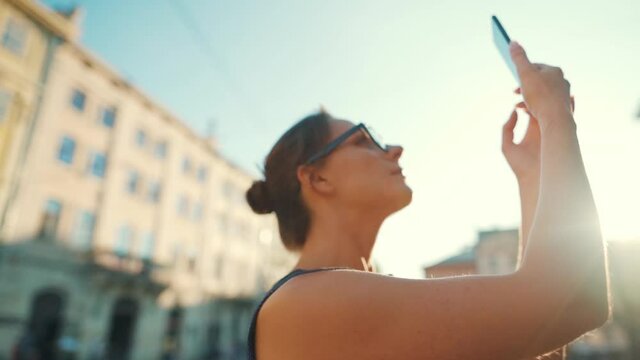 Woman stands on an old street and takes a photo or video on a smartphone at sunset. Slow motion