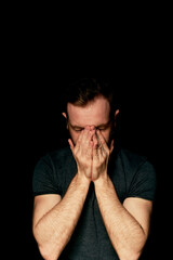 Naklejka premium A man on a black background covers his face with his hands. The atmosphere of hopelessness,dejection