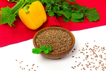 Red lentils seeds in wooden bowl and fresh vegetables on table cloth. Organic agriculture concept
