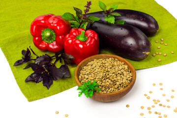 Red lentils seeds in wooden bowl and fresh vegetables on table cloth. Organic agriculture concept