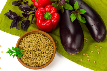 Red lentils seeds in wooden bowl and fresh vegetables on table cloth. Organic agriculture concept