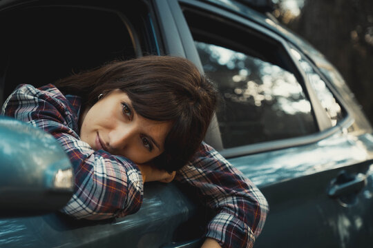 Portrait of a young woman with fair skin and brown hair looking through the rear view mirror of her parked car leaning her head on her man leaning out of the car's lowered window