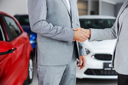 Cutout picture of car seller shaking hands with buyer while standing in car salon.
