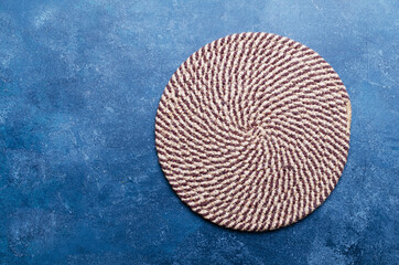 Round knitted  napkin of jute on blue board.