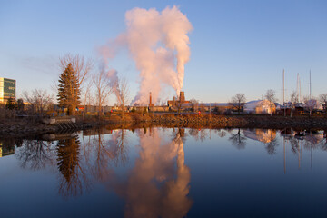 Fuming industrial buildings and their reflection in the Louise Basin during a sunny late Fall early morning, Quebec City, Quebec, Canada