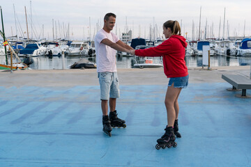 Young beautiful couple roller skating in skate park next to the amazing port in summer.Friendship...