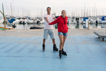 Young happy couple roller skating in skate park next to the beautiful port in summer.Friendship sport and fitness lifestyle concept.